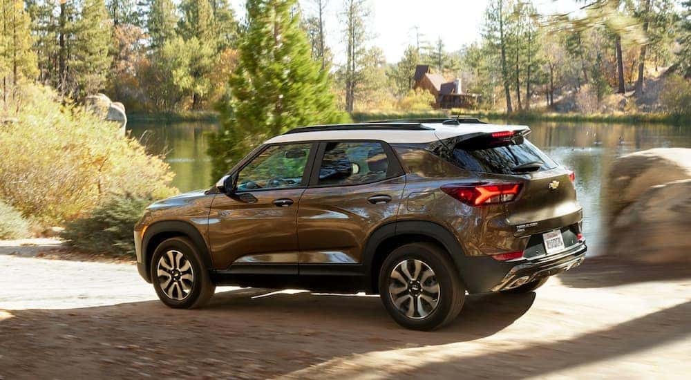 A brown and white 2021 Chevy Trailblazer is driving on a dirt road past a pond.