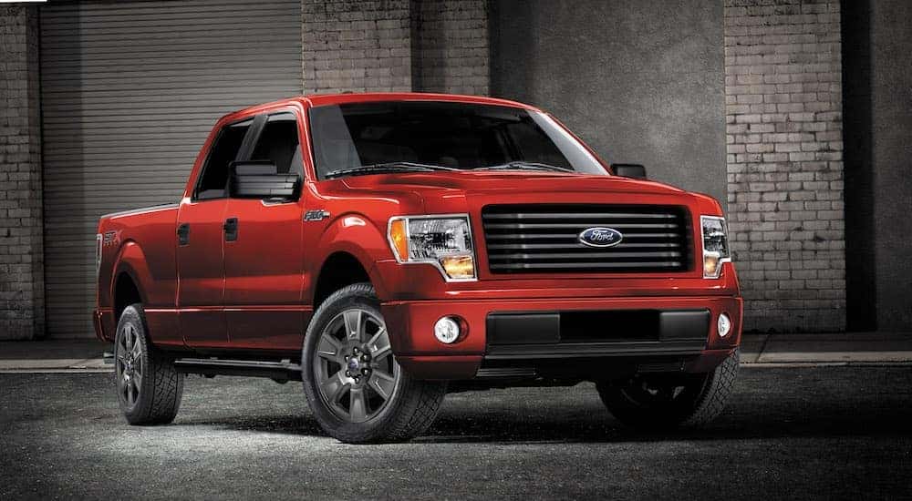 A red 2014 Ford F-150 is parked in front of garage doors at night.