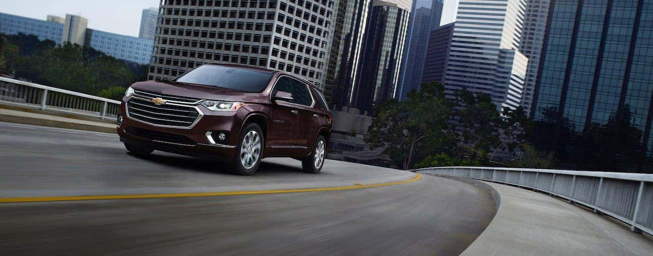 A burgundy 2020 Chevy Traverse is driving away from a city after winning the 2020 Chevy Traverse vs 2020 Honda Pilot comparison.