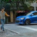 A couple is walking past a blue 2020 Chevy Sonic on a city street after leaving an Atlanta Chevy dealer.