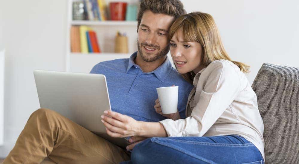 A couple is looking at a laptop while in their living room.