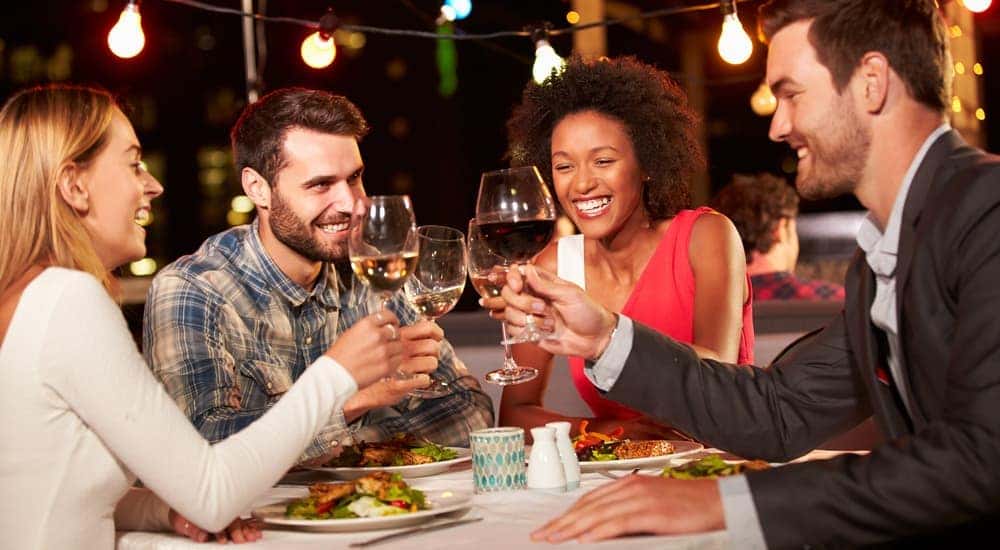 Four friends are drinking wine outdoors at a restaurant at night.