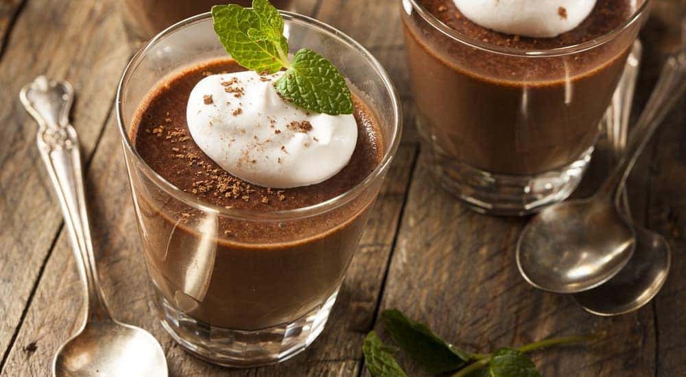 Cups of chocolate mousse are on a wooden table.