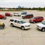 The 75th Anniversary collection of Chevy Suburbans over the years are parked in a large parking lot showing the evolution of Chevy SUV models.