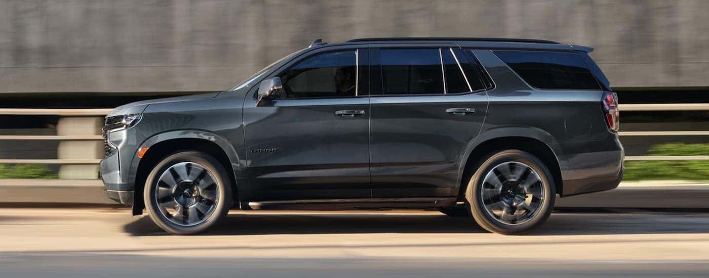 A grey 2021 Chevy Tahoe is driving past a railing and grey building.