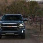 A gray 2016 Chevy Silverado 1500 is shown from the front in front of a horse farm at sunset.