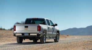 A great used Chevy truck to find, a silver 2016 Chevy Silverado 1500, is facing away on a desert highway towards distant mountains.