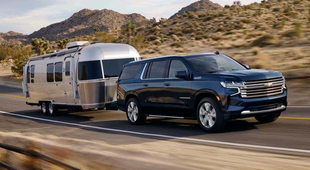 A black 2021 Chevy Suburban, which is the largest of the Chevy SUVS, is towing an Airstream past hills.