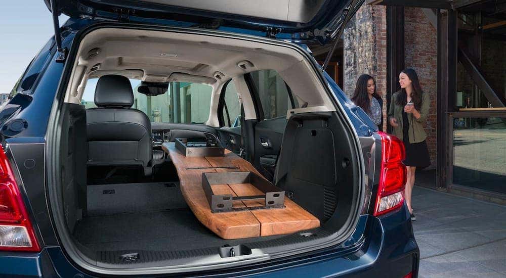Two women are walking towards the cargo area of a blue 2020 Chevy Trax, which has a table in it.
