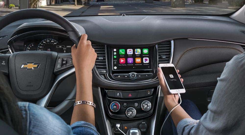 A closeup shows someone connecting their phone to a 2020 Chevy Trax's infotainment center while another person drives.