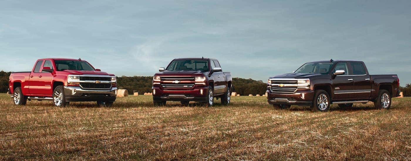 Three red 2016 Used Chevy Silverados are parked in a field.
