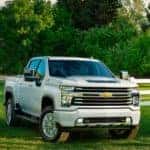 A popular Chevy diesel truck, a white 2021 Chevy Silverado 2500HD is parked on the grass next to a white fence.
