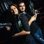 A man and woman are standing back to back holding up laser tag guns.