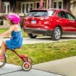 A red 2018 Chevy Equinox is parked in a driveway with a child on a tricycle behind it.