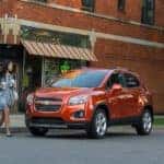 A popular used SUV for sale, a orange 2016 Chevy Trax, is parked outside of a natural food store.