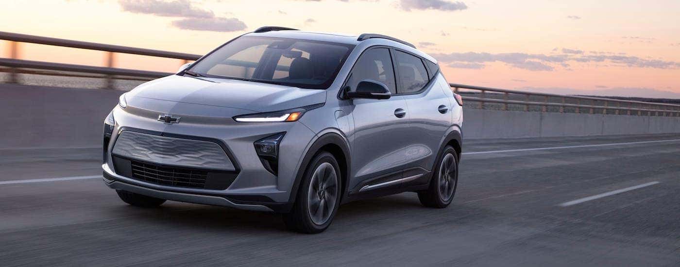 A silver 2022 Chevy Bolt EUV is driving on a highway at dusk.