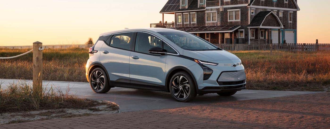 A pale blue Chevy EV, a 2022 Chevy Bolt EV, is parked in front of a beach house.