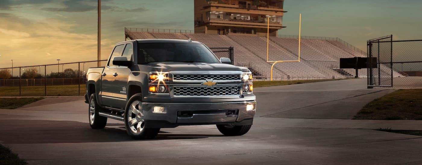 A popular used Chevy truck, a black 2016 Chevy Silverado 1500, is parked in front of a football field.
