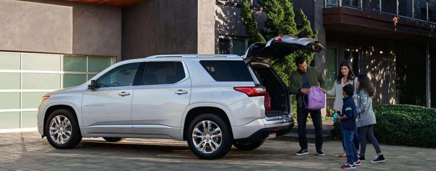 A silver 2021 Chevy Traverse is shown from the side with a father putting a back pack in the trunk.