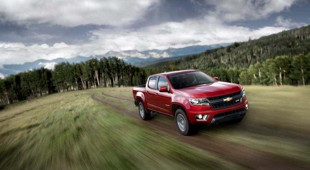 A red 2015 Chevy Colorado is driving on a dirt trail in front of trees.