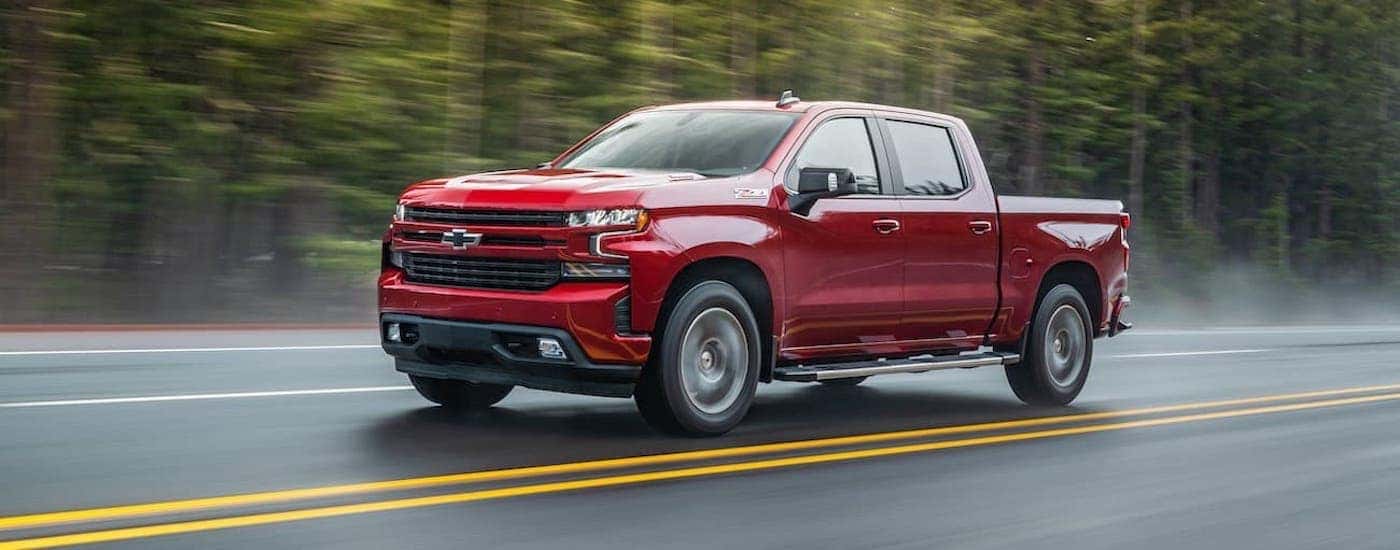 A red 2021 Chevy Silverado 1500 is driving past a forest of pine trees.