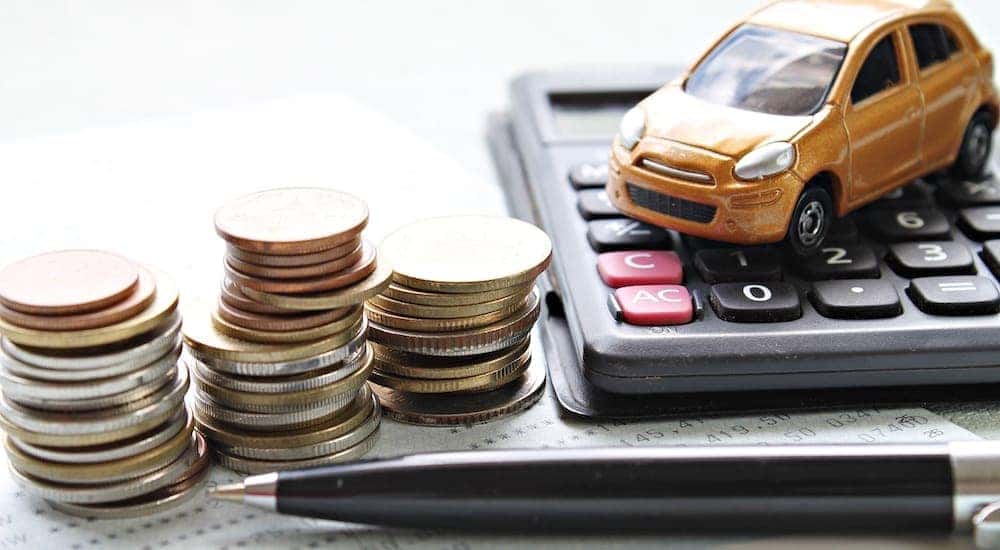 A pile of coins, toy car, pen and calculator sit on a desk.