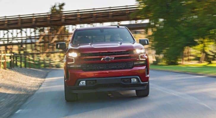 A red 2020 Chevy Silverado is driving under a train trestle.