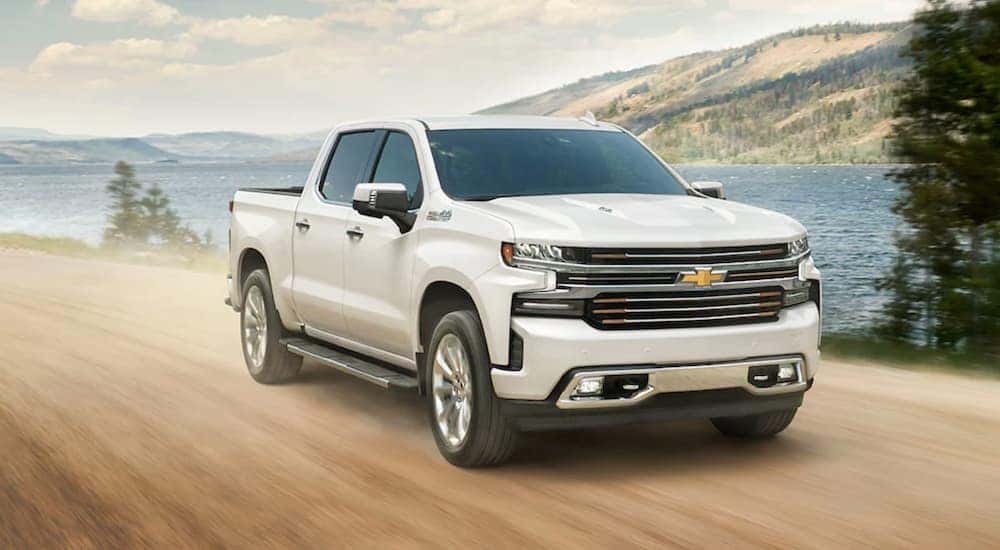 A white 2021 Chevy Silverado 1500 is drivign on a dirt road past a lake.