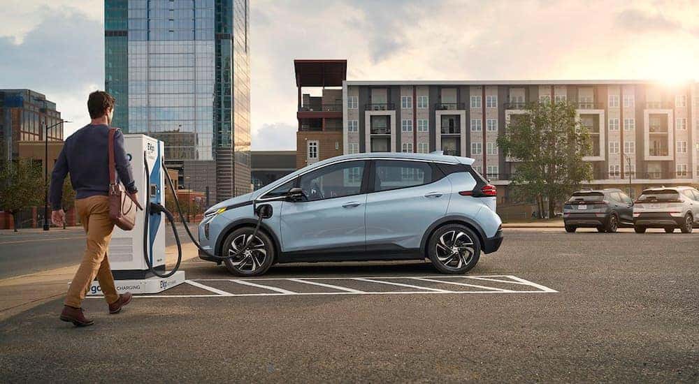 One of the most popular new Chevy vehicles in stock, a pale blue 2022 Chevy Bolt EV, is shown at a charging station.