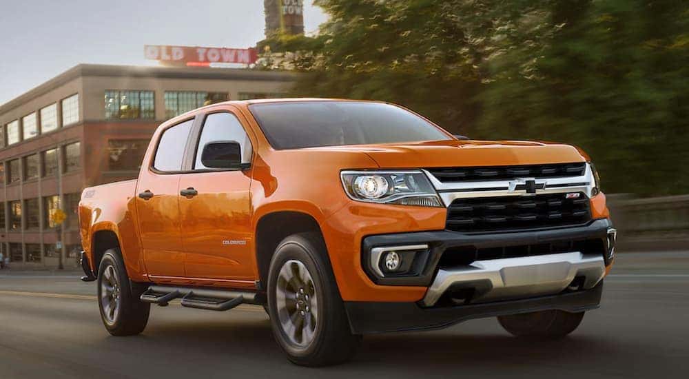An orange 2021 Chevy Colorado is shown from the front driving through a city.