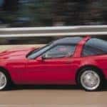 A red 1990 Chevy Corvette ZR1 is shown from the side driving on a highway past used Chevrolet dealers in Atlanta.