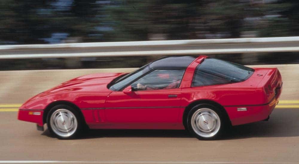 A red 1990 Chevy Corvette ZR1 is shown from the side driving on a highway past used Chevrolet dealers in Atlanta.
