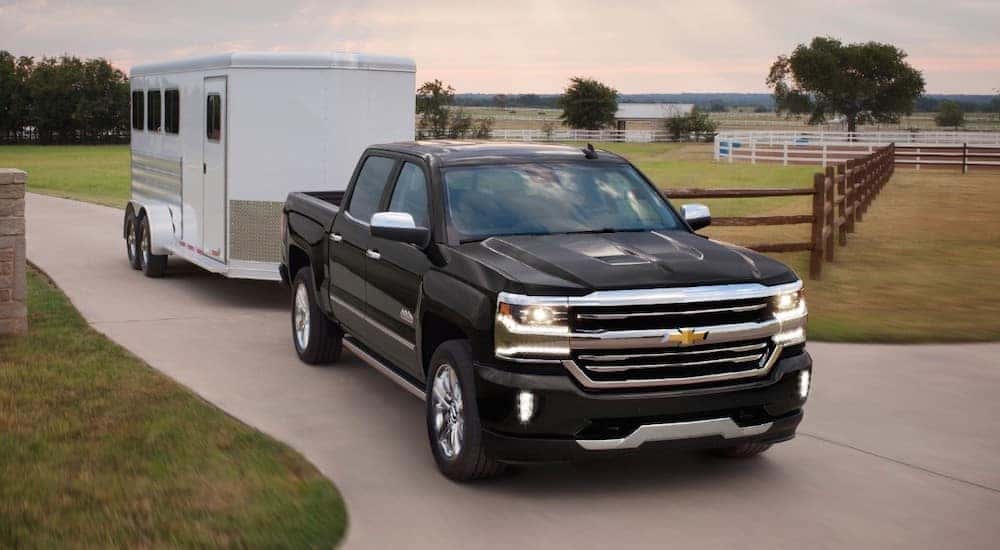 A black 2018 certified pre-owned Chevy Silverado 1500 is shown towing a horse trailer.