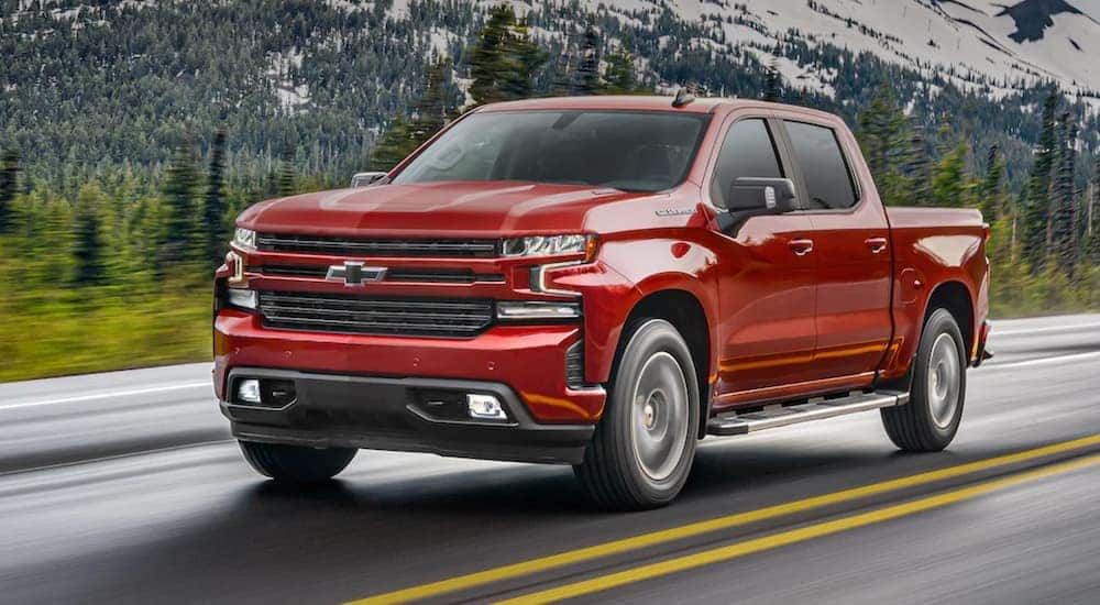 A red certified pre-owned Chevy truck, the 2021 Chevy Silverado 1500, is shown driving on a highway.