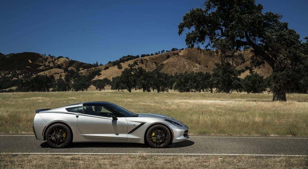 A silver Certified Pre-Owned 2014 Chevy Corvette is shown from the side parked in a field.