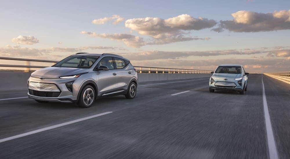 A silver 2022 Chevy Bolt EUV and a light blue Bolt EV are shown driving down a highway.