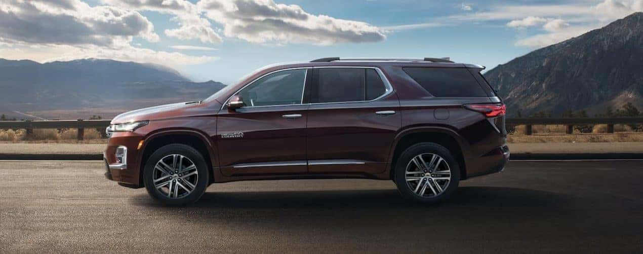 A maroon 2022 Chevy Traverse High Country is shown from the side parked in front of a mountain range.