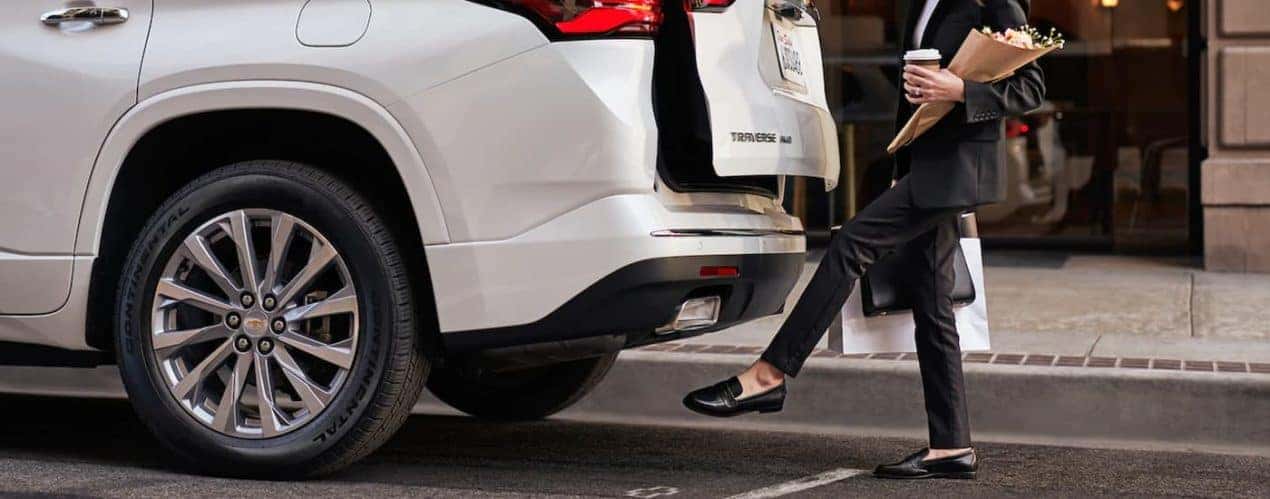 A woman is shown using the touch free lift gate on a white 2022 Chevy Traverse.