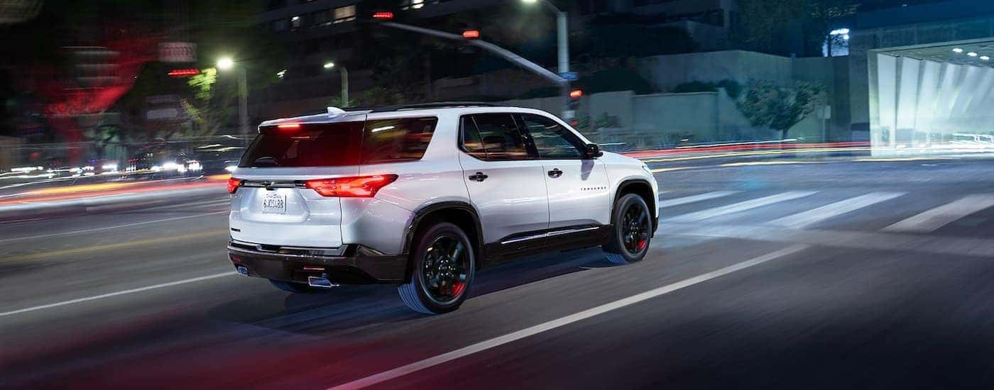 A silver 2022 Chevy Traverse is shown from the side driving through a city at night.
