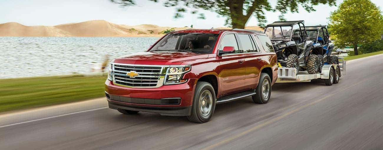 A red 2020 Chevy Tahoe is shown towing UTVs on an open road.