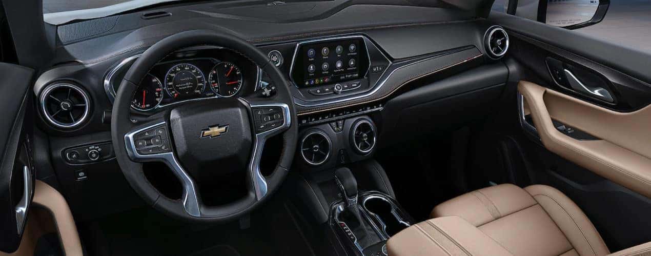 The black and tan interior of a 2022 Chevy Blazer shows the steering wheel and infotainment screen.