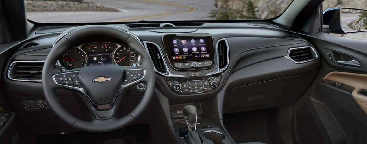 The black interior of a 2022 Chevy Equinox shows the steering wheel and infotainment screen during a 2022 Chevy Equinox vs 2022 Ford Escape comparison.