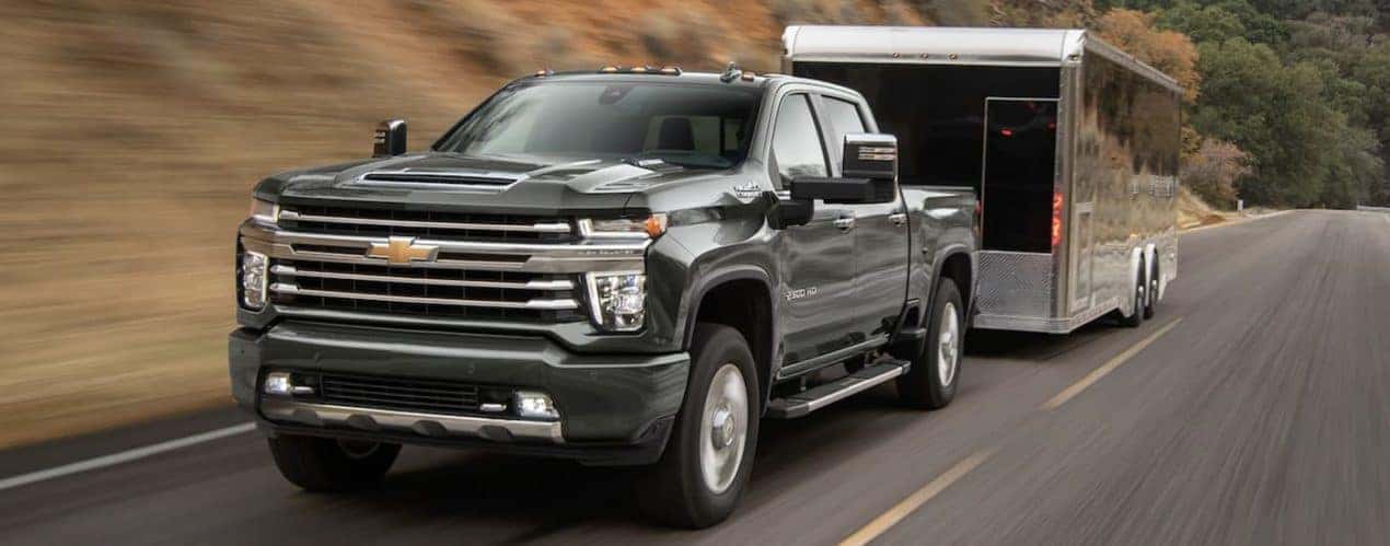 A black 2022 Chevy 2500 HD is shown from the front towing a closed trailer on an open road.