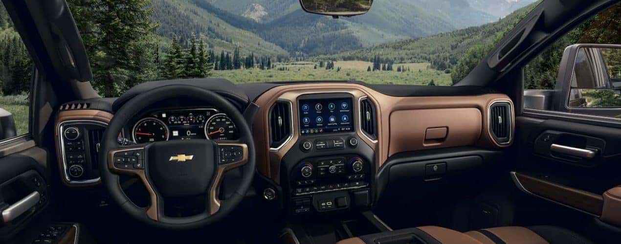 The brown and black interior of a 2022 Chevy Silverado 2500 HD shows the steering wheel and infotainment screen.