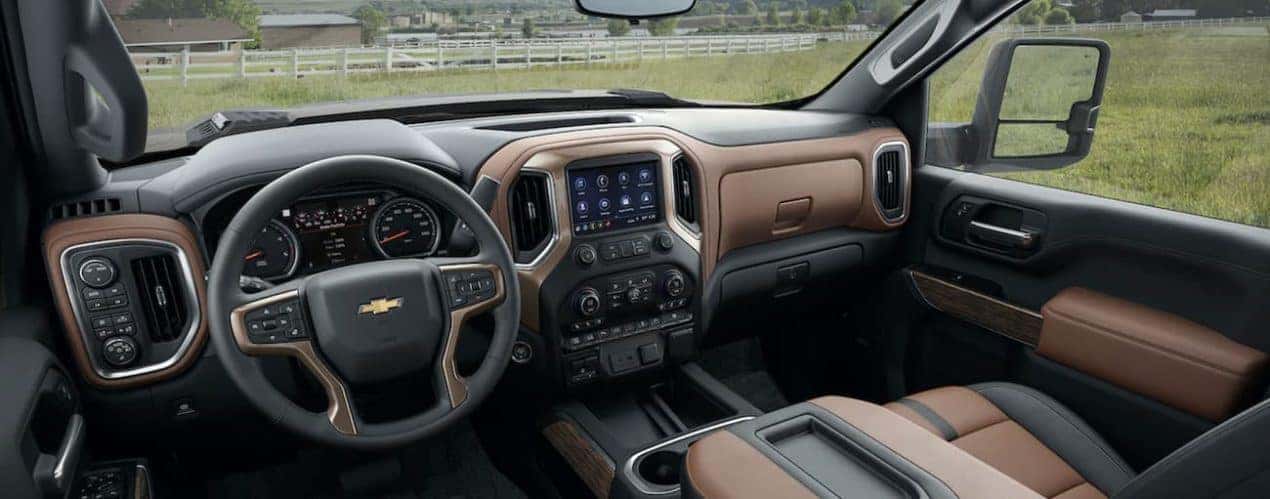 The black and brown interior of a 2022 Chevy 2500 HD shows the steering wheel and infotainment screen.