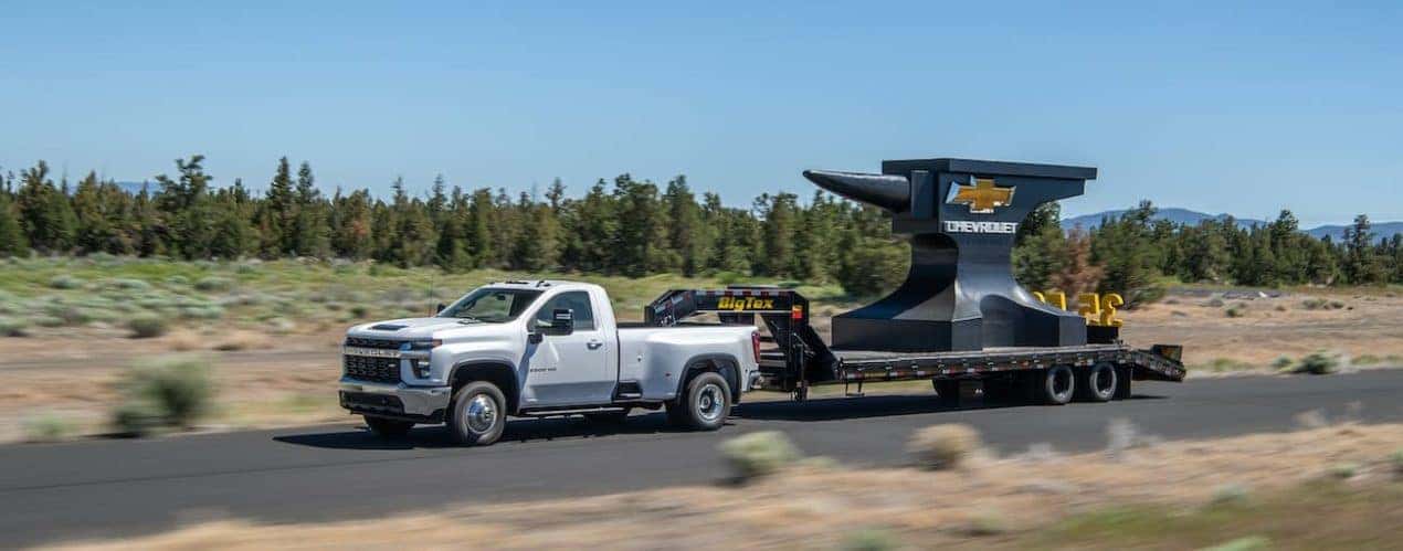A white 2022 Chevy Silverado 3500 HD is shown towing a giant anvil on a trailer.