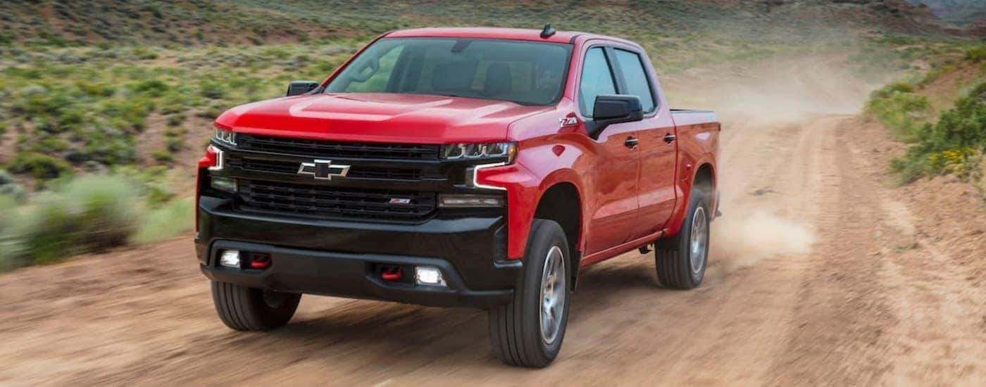 A red 2020 Chevy Silverado Trailboss Z71 is shown driving on a dirt road.
