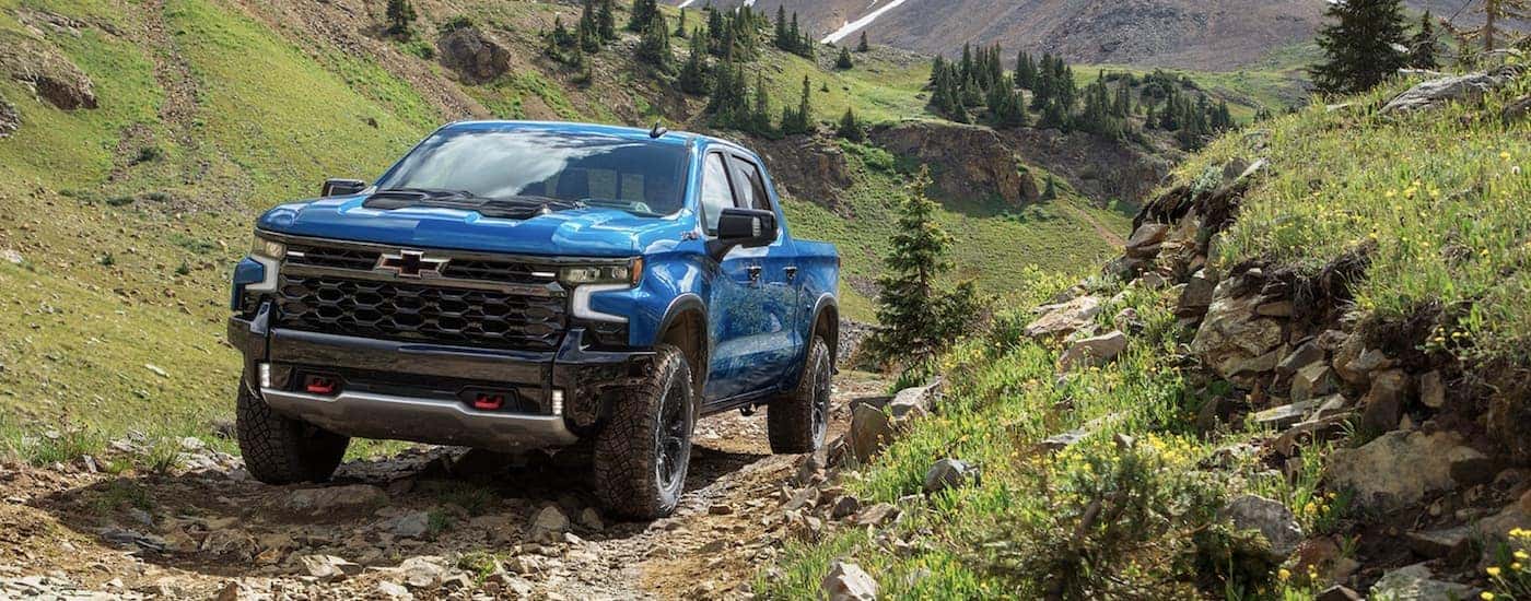 A blue 2022 Chevy Silverado 1500 ZR2 is shown driving on a dirt road after leaving a lifted truck dealer.