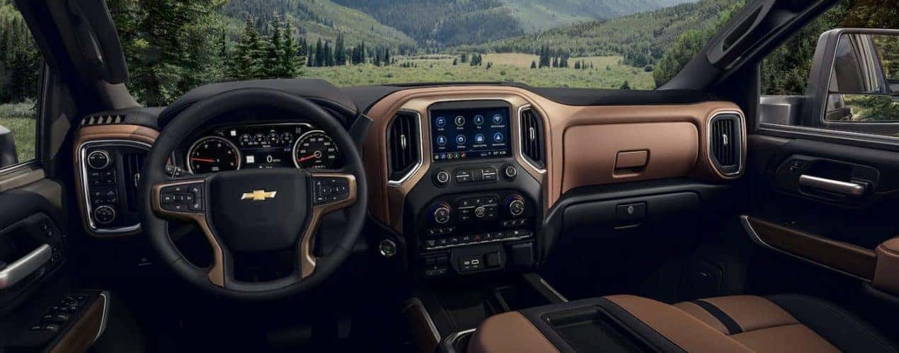 The black and brown interior of a 2022 Chevy Silverado 2500 HD Custom shows the steering wheel and infotainment screen.