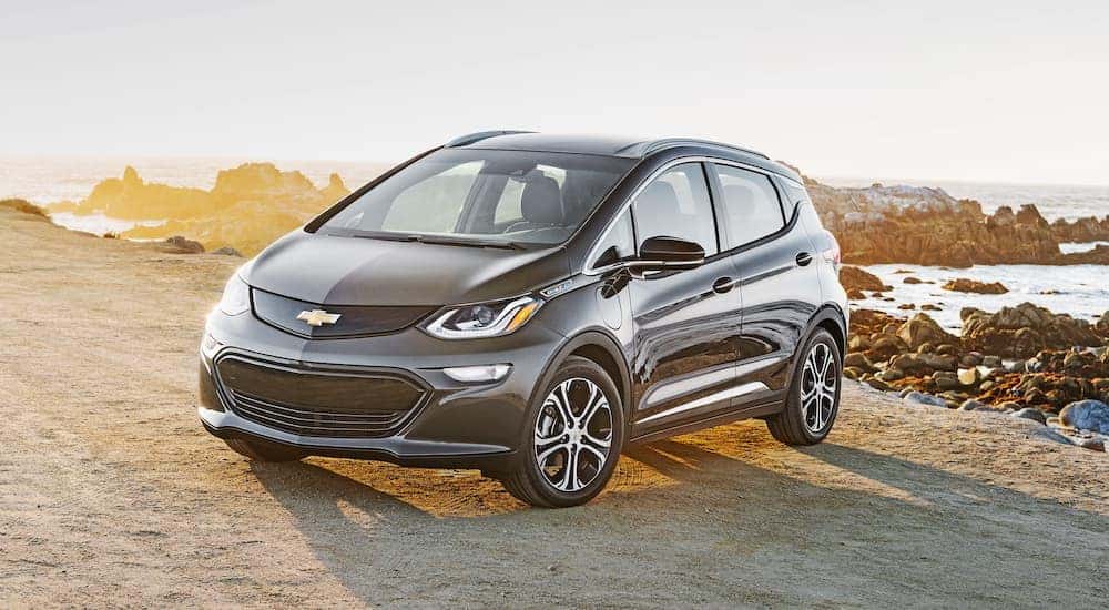 A silver 2018 Chevy Bolt EV is shown from the side parked in front of a body of water.